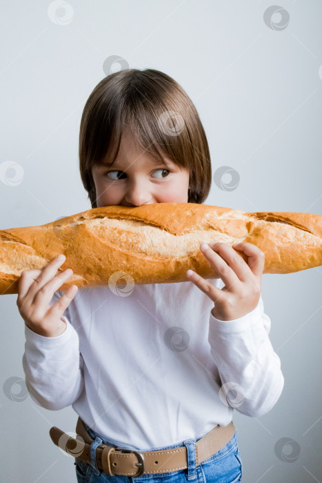 Скачать Маленький кавказский ребенок игриво держит в руках большой багет на белом фоне фотосток Ozero