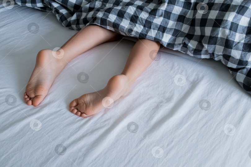 Скачать Детские ножки под клетчатым одеялом на белой кровати фотосток Ozero