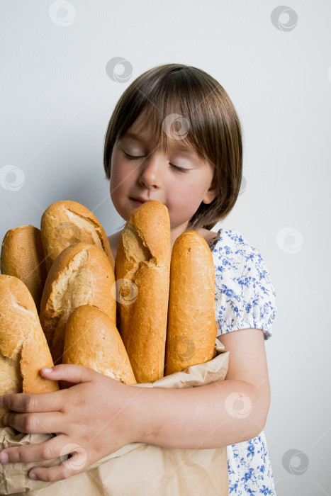 Скачать Маленький кавказский ребенок держит в руках пакет со свежими багетами и удовлетворенно закрывает глаза фотосток Ozero