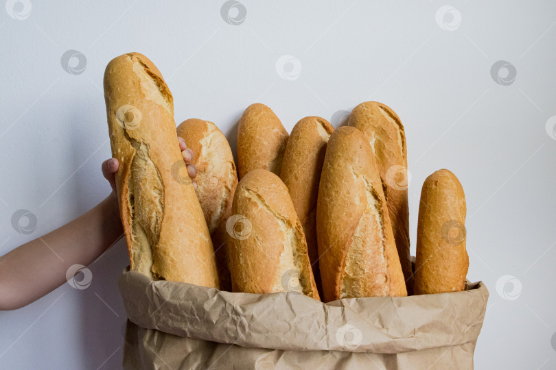 Скачать Изобилие свежеиспеченных багетов в коричневом бумажном пакете, сделанном рукой кавказского ребенка фотосток Ozero