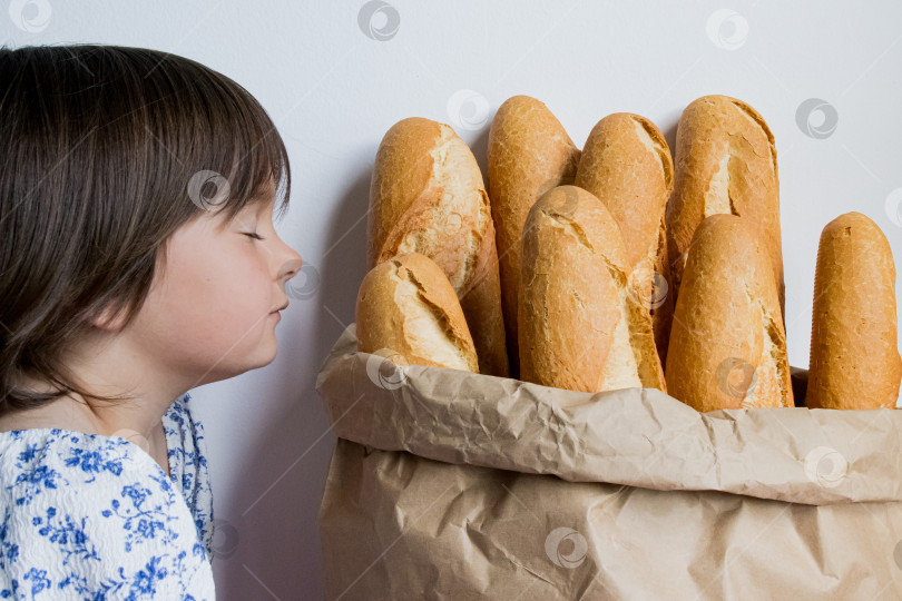 Скачать Кавказский ребенок со свежими багетами в бумажном пакете на белом фоне фотосток Ozero