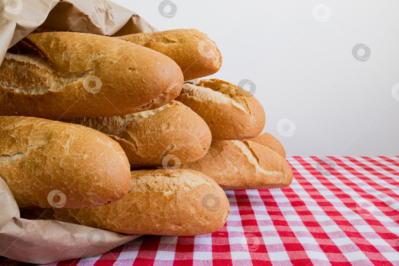 Скачать Свежие багеты в коричневом бумажном пакете на красной клетчатой скатерти фотосток Ozero