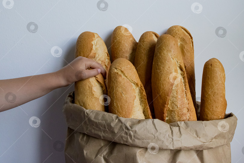 Скачать Детская ручка тянется за свежеиспеченными багетами в бумажном пакете фотосток Ozero