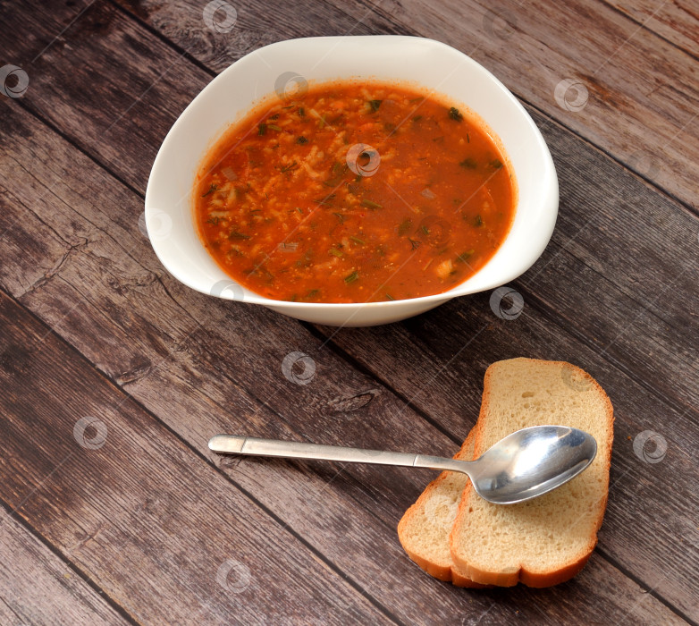 Скачать Кавказский острый суп Харчо в глубокой тарелке и два кусочка пшеничного хлеба ложкой выкладывают на деревянный стол. фотосток Ozero