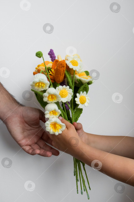 Скачать Ребенок и взрослый держат в руках красочный букет цветов, связанный крючком, на белом фоне. Концепция дня отцов фотосток Ozero