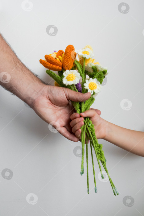 Скачать Взрослая рука вручает ребенку букет цветов, связанный крючком, на белом фоне. Концепция дня отцов фотосток Ozero