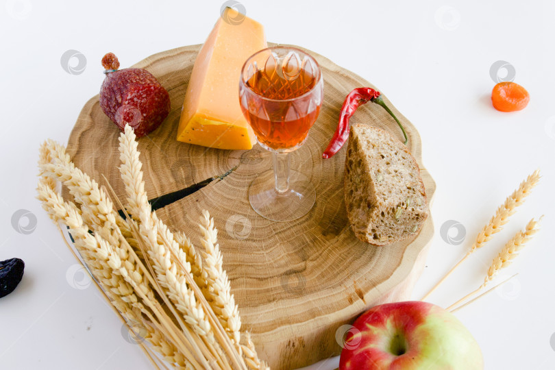 Скачать натюрморт с яблоками и другими продуктами, колосьями пшеницы на дубовой подставке и бокалом домашней крепкой настойки на кедровых орехах фотосток Ozero