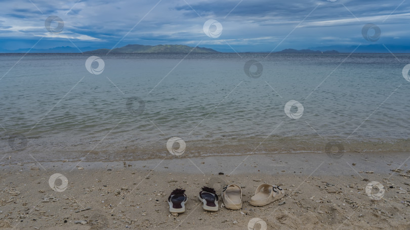 Скачать Две пары шлепанцев на песчаном пляже у кромки воды. фотосток Ozero