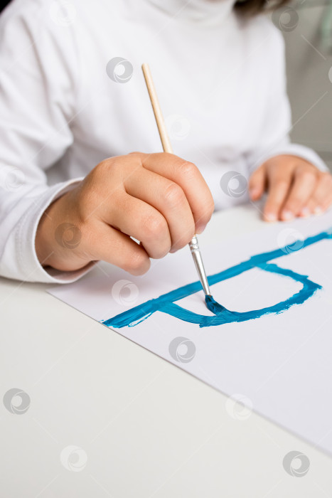 Скачать Маленький ребенок рисует синей кистью на бумаге, крупный план руки и художественная деятельность фотосток Ozero