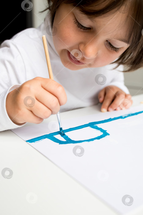 Скачать Маленький кавказский ребенок рисует дома синей акварелью фотосток Ozero