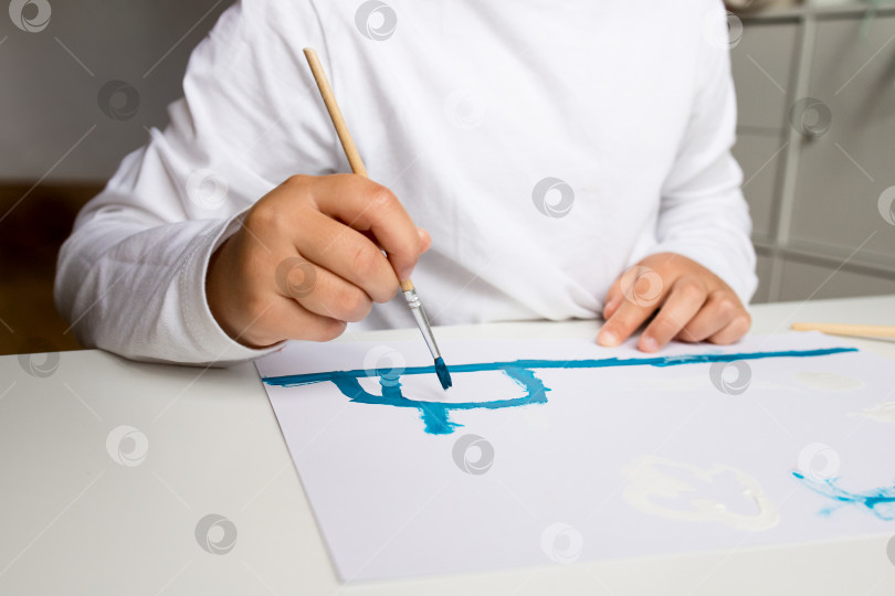 Скачать Ребенок рисует синим на белой бумаге с кистью в руке фотосток Ozero