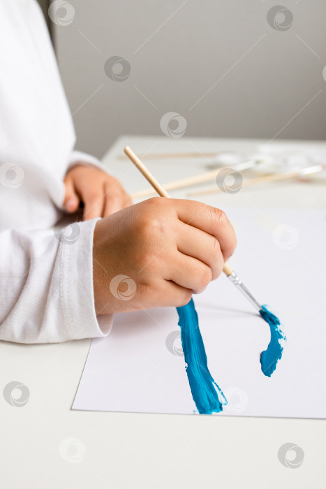 Скачать Маленький кавказский ребенок рисует голубым мазком на белой бумаге фотосток Ozero