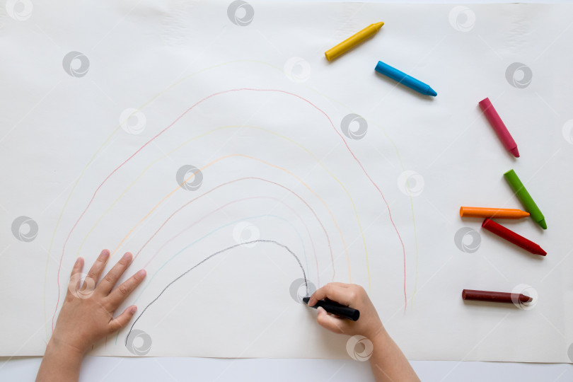 Скачать Ребенок рисует разноцветную радугу цветными карандашами на бумаге фотосток Ozero