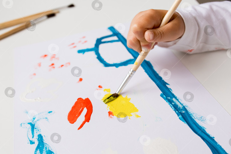 Скачать Ребенок создает красочную абстрактную картину кистью на белой бумаге фотосток Ozero