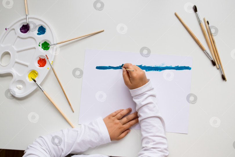Скачать Ребенок рисует синим цветом на холсте с помощью кистей и палитры фотосток Ozero
