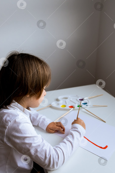 Скачать Маленький кавказский ребенок рисует акварелью за белым столом фотосток Ozero