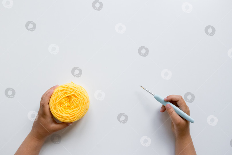 Скачать Детские ручки, связанные крючком желтой пряжей и синим крючком на белом фоне фотосток Ozero