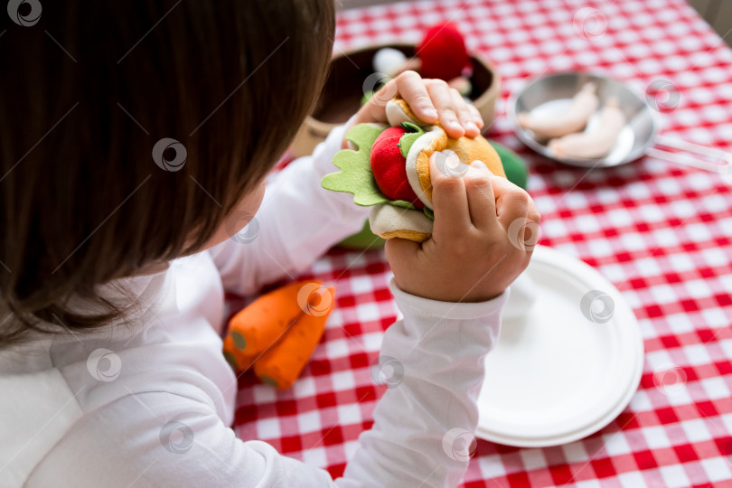 Скачать Ребенок вовлекается в творческую игру с игрушечной едой за клетчатым столом фотосток Ozero
