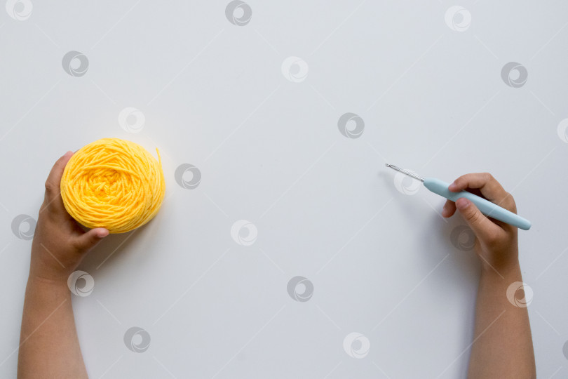 Скачать Детские ручки с желтой пряжей и крючком для вязания крючком на белом фоне фотосток Ozero