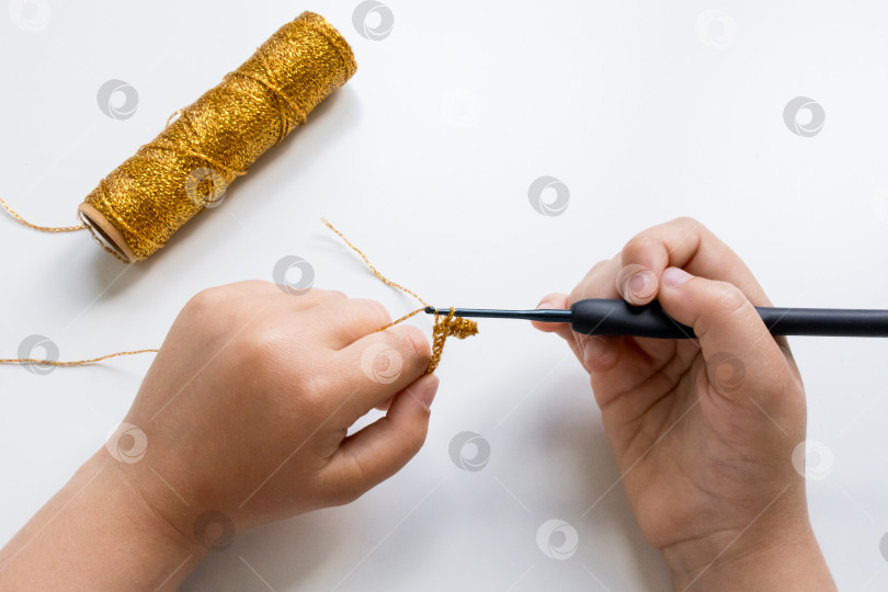 Скачать Детское вязание крючком золотой пряжей и крючком на белой поверхности крупным планом фотосток Ozero