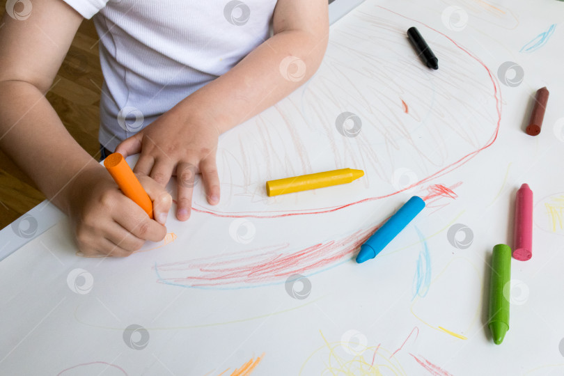 Скачать Маленький ребенок рисует разноцветными мелками на белой бумаге фотосток Ozero