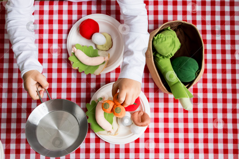Скачать Ребенок играет с разноцветными фетровыми овощами на красной клетчатой скатерти фотосток Ozero