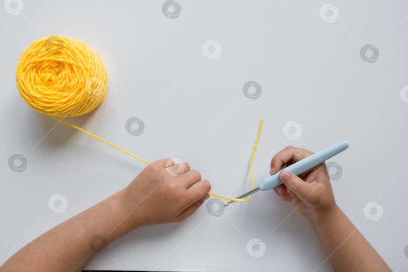 Скачать Детские ручки вяжут крючком из желтой пряжи на белом фоне фотосток Ozero