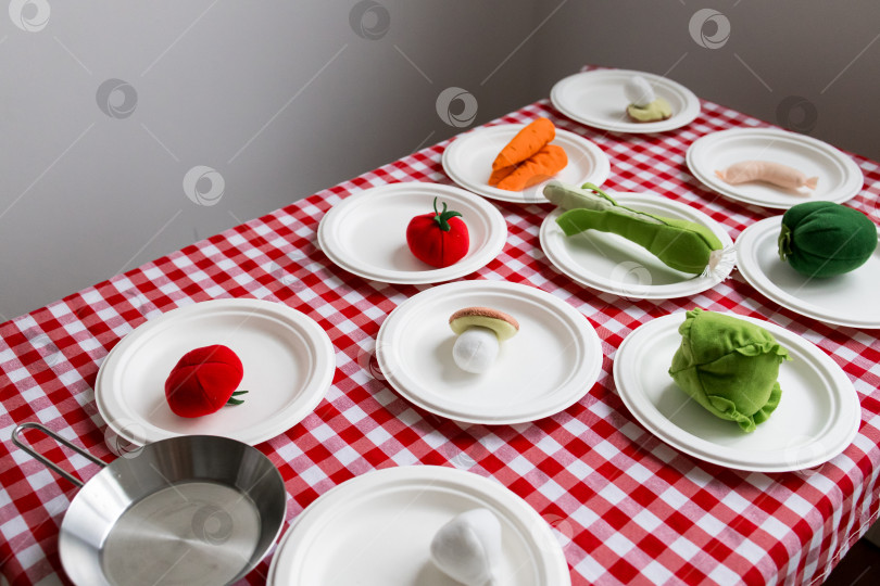 Скачать Разноцветные плюшевые овощи на клетчатой скатерти с белыми тарелками фотосток Ozero