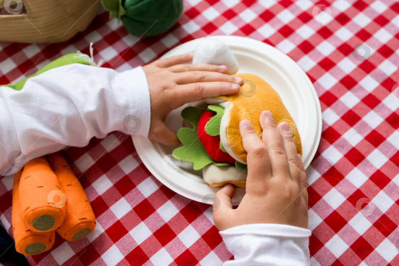 Скачать Ребенок играет с игрушечным бутербродом на красной клетчатой скатерти фотосток Ozero