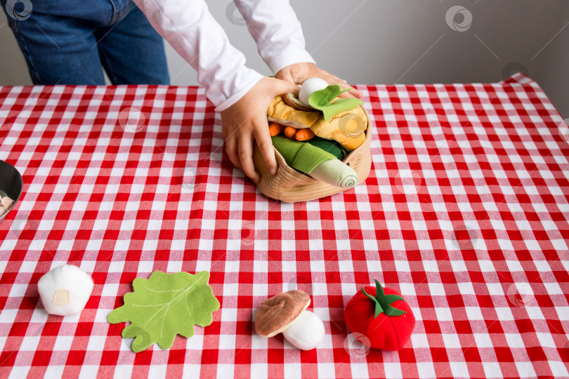 Скачать Ребенок играет с игрушечными овощами на красной клетчатой скатерти фотосток Ozero