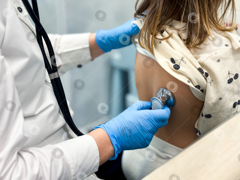 Скачать Детский врач осматривает молодую пациентку с помощью стетоскопа в медицинской клинике фотосток Ozero