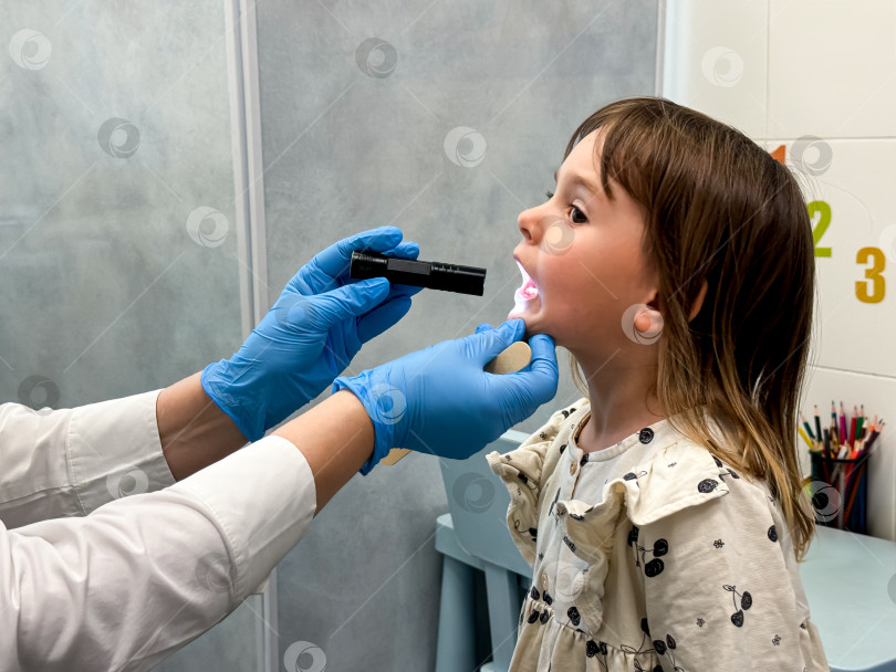 Скачать Молодая кавказская девушка проходит осмотр горла врачом в медицинском кабинете фотосток Ozero