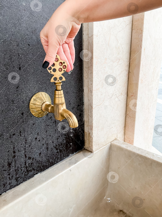 Скачать Женская рука поворачивает богато украшенную ручку наружного крана над мраморной раковиной фотосток Ozero