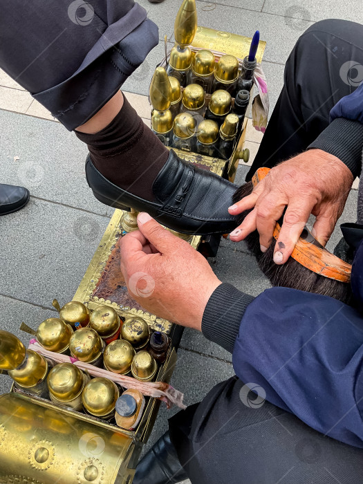 Скачать Сцена чистки обуви взрослым мужчиной-кавказцем с золотыми бутылочками полироли на улице фотосток Ozero