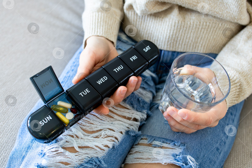 Скачать Крупный план человека, держащего органайзер для таблеток и стакан воды на рваных джинсах фотосток Ozero