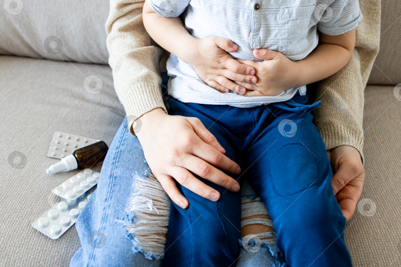 Скачать Молодой кавказский ребенок с болью в животе, которого взрослая женщина утешает на кушетке с лекарствами фотосток Ozero