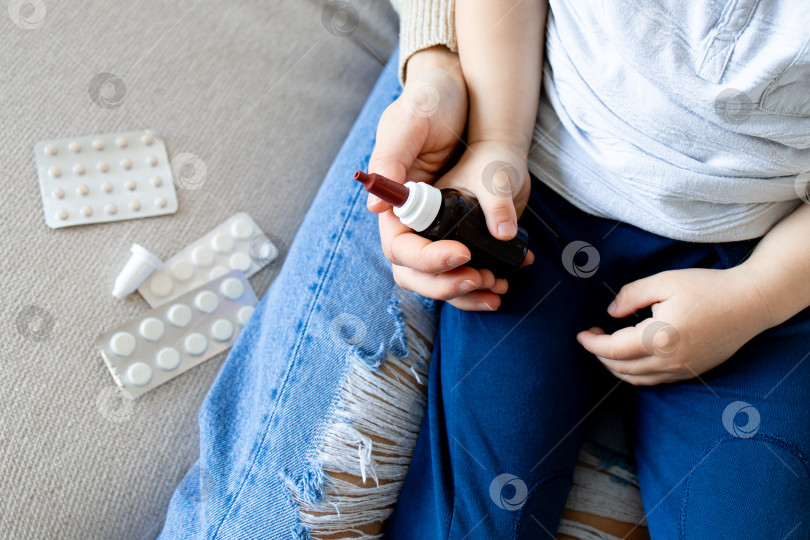 Скачать Маленький ребенок белой расы держит рядом бутылочку с лекарством и таблетками фотосток Ozero