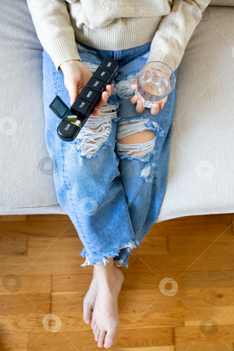 Скачать Взрослая кавказская женщина принимает лекарства с помощью органайзера для таблеток и стакана с водой фотосток Ozero