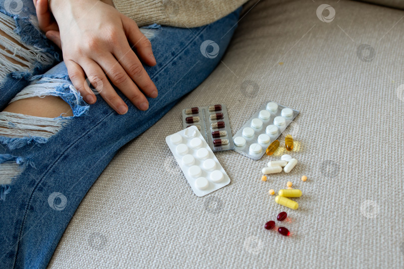 Скачать Молодая белая женщина в повседневном наряде с разнообразными таблетками на диване фотосток Ozero