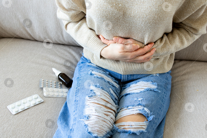 Скачать Взрослая белая женщина испытывает боль в животе, лежа на диване с лекарствами рядом фотосток Ozero