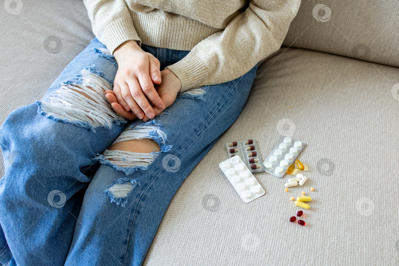 Скачать Небрежно одетая женщина сидит на диване с разложенными на витрине лекарствами фотосток Ozero
