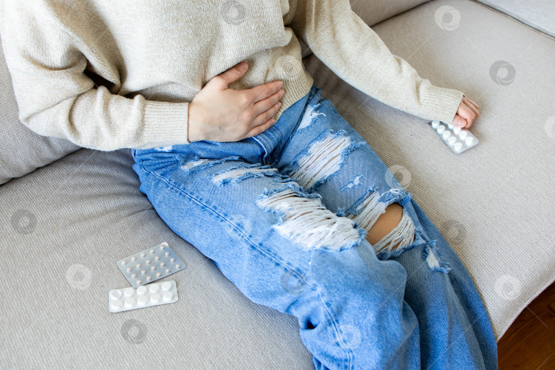 Скачать Женщина, испытывающая боль в животе и принимающая таблетки на диване. Молодой мужчина белой расы фотосток Ozero