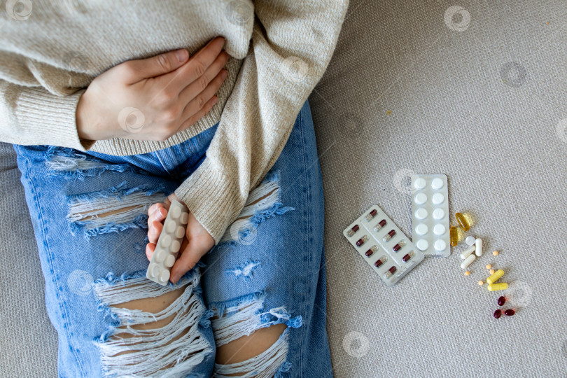 Скачать Молодая белая женщина испытывает дискомфорт от приема таблеток на диване фотосток Ozero