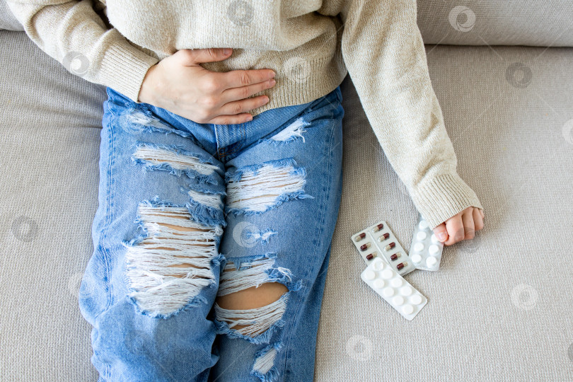 Скачать Молодая белая женщина с болью в животе держит лекарство на диване фотосток Ozero