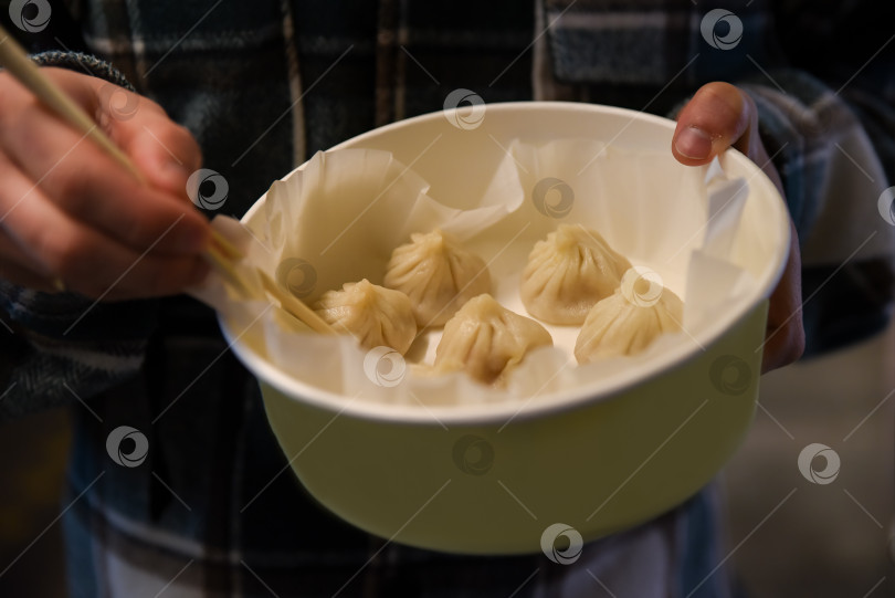 Скачать Крупный план китайских пельменей с крабами и свининой в миске, которую держит турист на старой улице Юйюань в Шанхае, с палочками для еды наготове, чтобы выбрать один из них. фотосток Ozero
