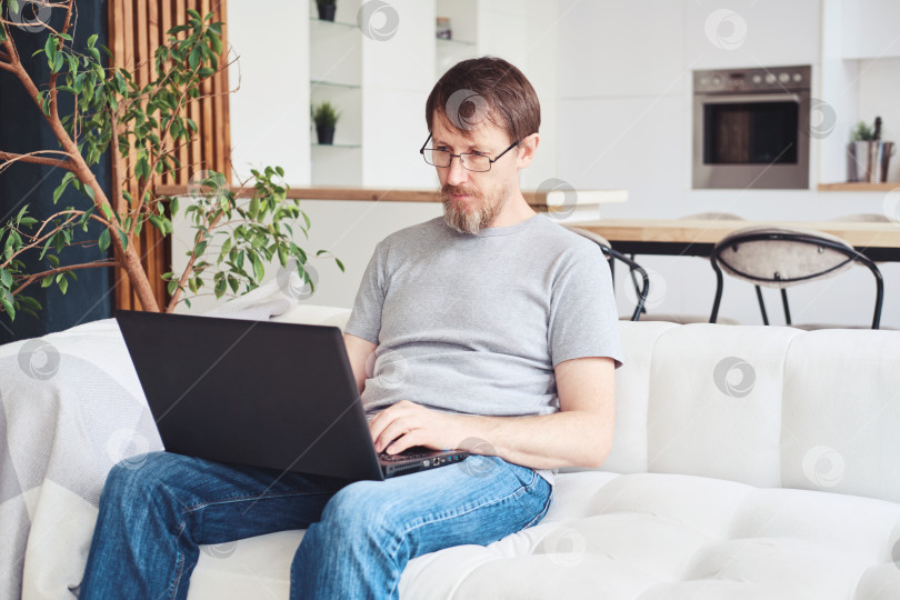 Скачать Счастливый бородатый мужчина, работающий в офисе, работает удаленно из дома. Пятидесятилетний мужчина пользуется ноутбуком. Онлайн-образование и работа фотосток Ozero