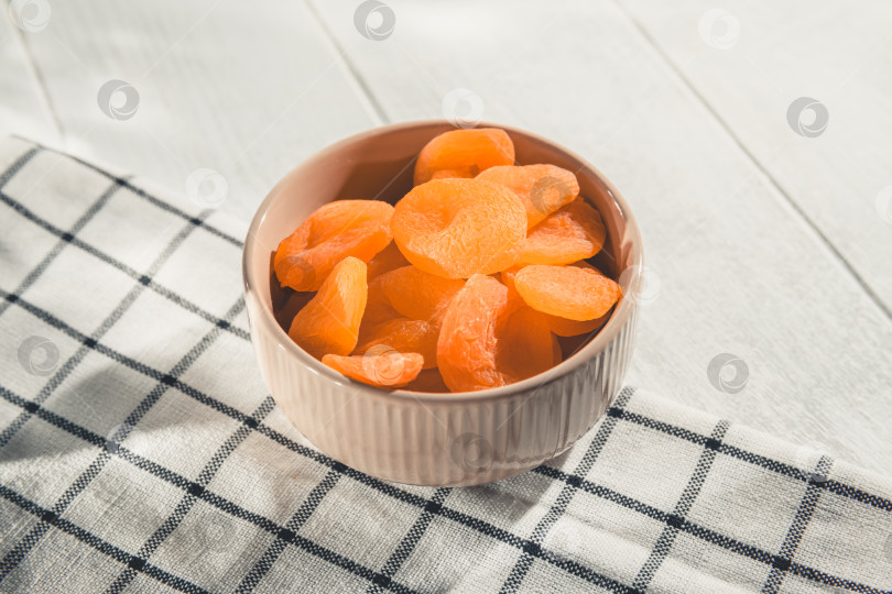 Скачать Наполненная курагой до краев. Бежевая тарелка накрыта клетчатой салфеткой. Благодаря яркому сочетанию цвета и текстуры эта полезная закуска подчеркивает естественную сладость и питательную ценность. фотосток Ozero