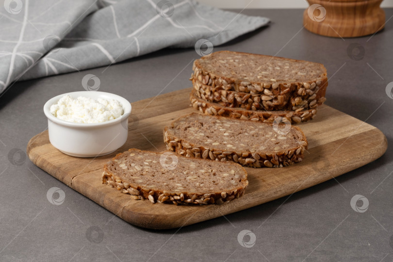 Скачать Вкусный цельнозерновой хлеб со сливочным творожным сыром на деревянной доске в современной кухонной обстановке фотосток Ozero