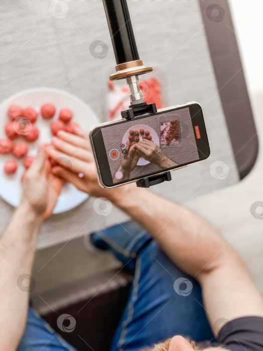 Скачать Мужчина готовит фрикадельки, записывая видео на смартфон фотосток Ozero