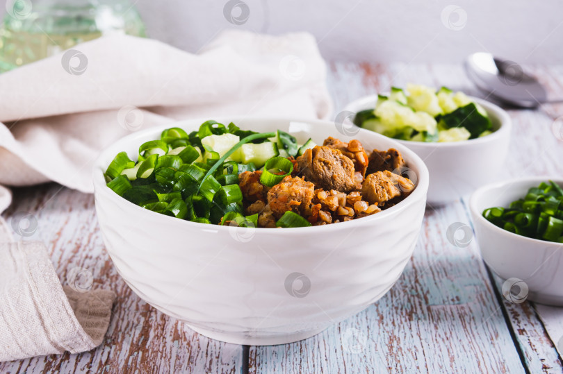 Скачать Гречневая каша с мясом, огурцом и зеленым луком в миске на столе фотосток Ozero